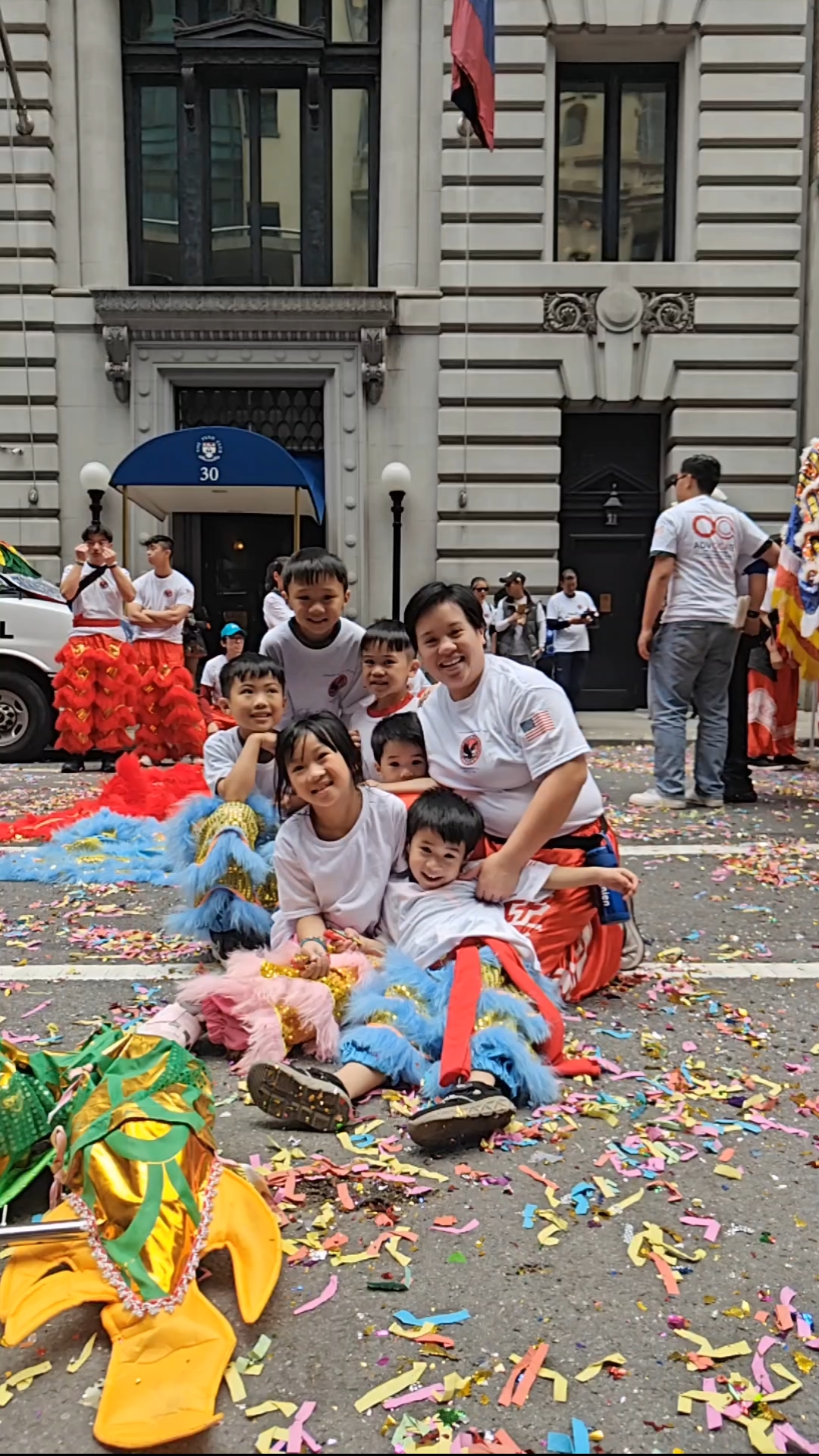 Young Bao Bao Lions performers and their coach sitting together in the confetti after a parade