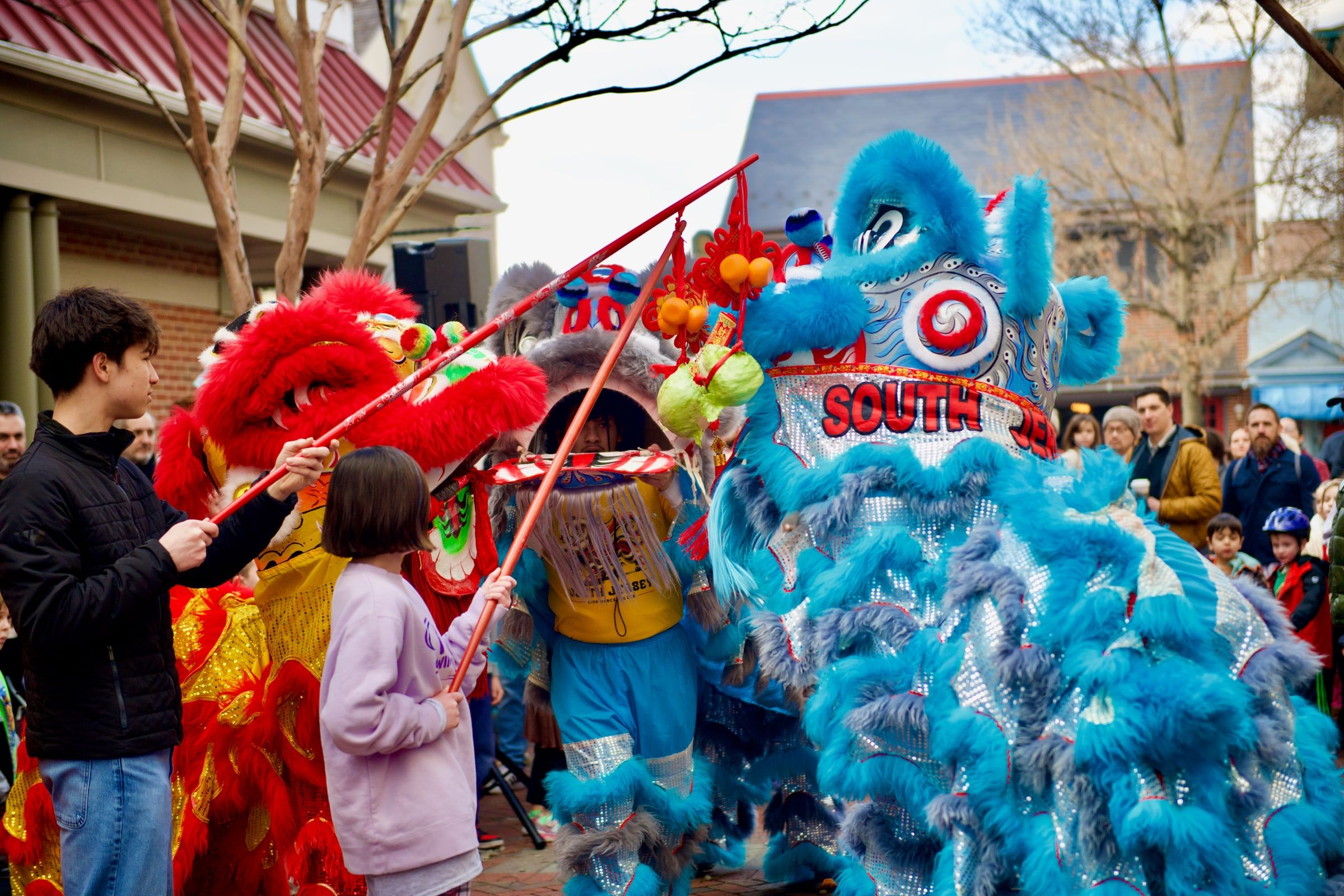 Children holding out lettuce on poles to feed a blue lion