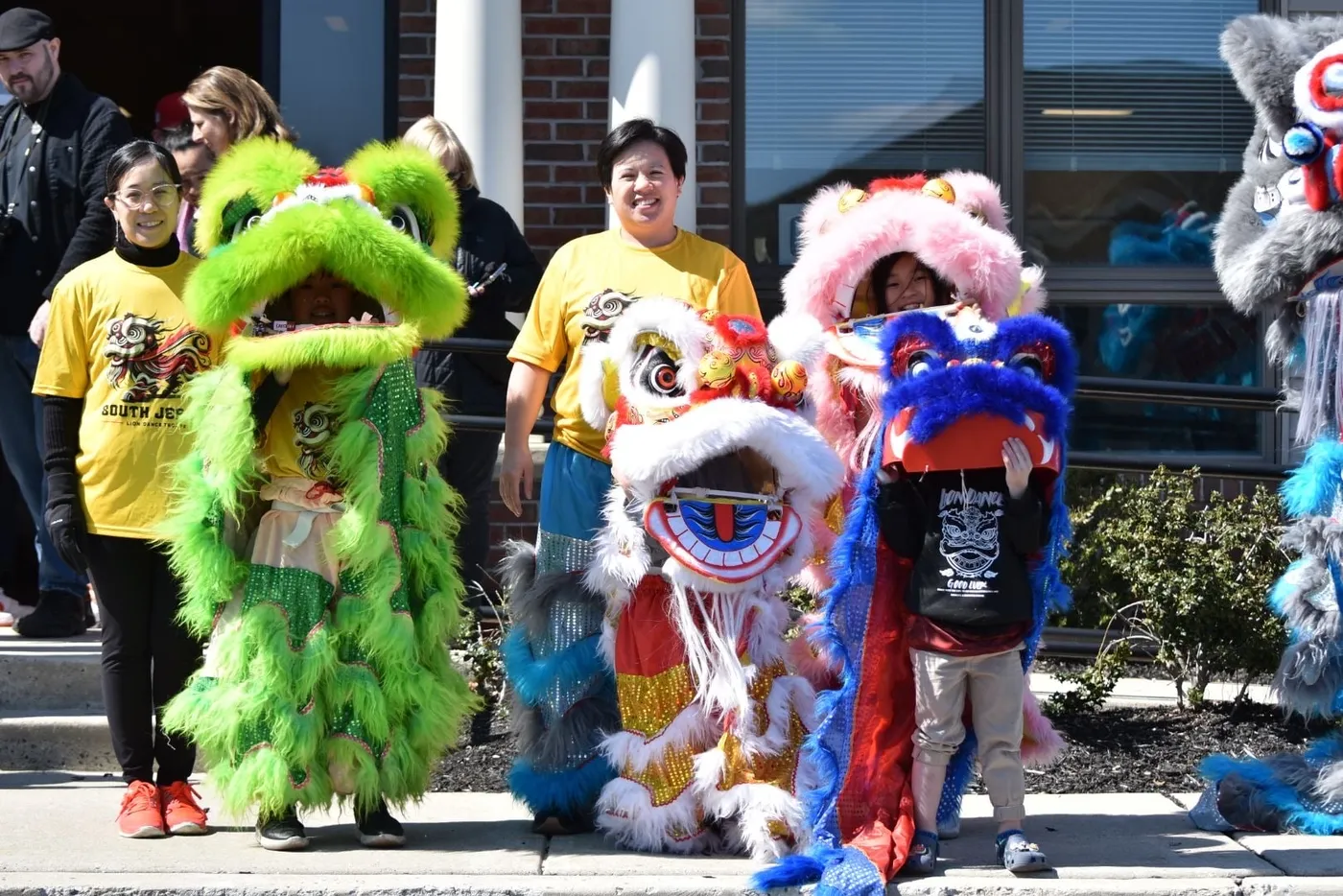 Two coaches standing with young students dressed in green, white and blue lion costumes