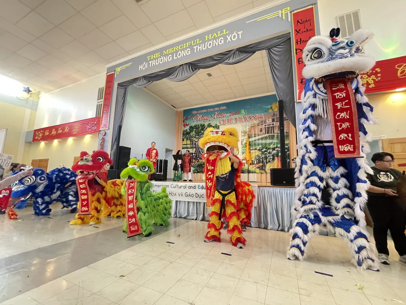 Lions holding red banners on stage at a cultural celebration in a community hall
