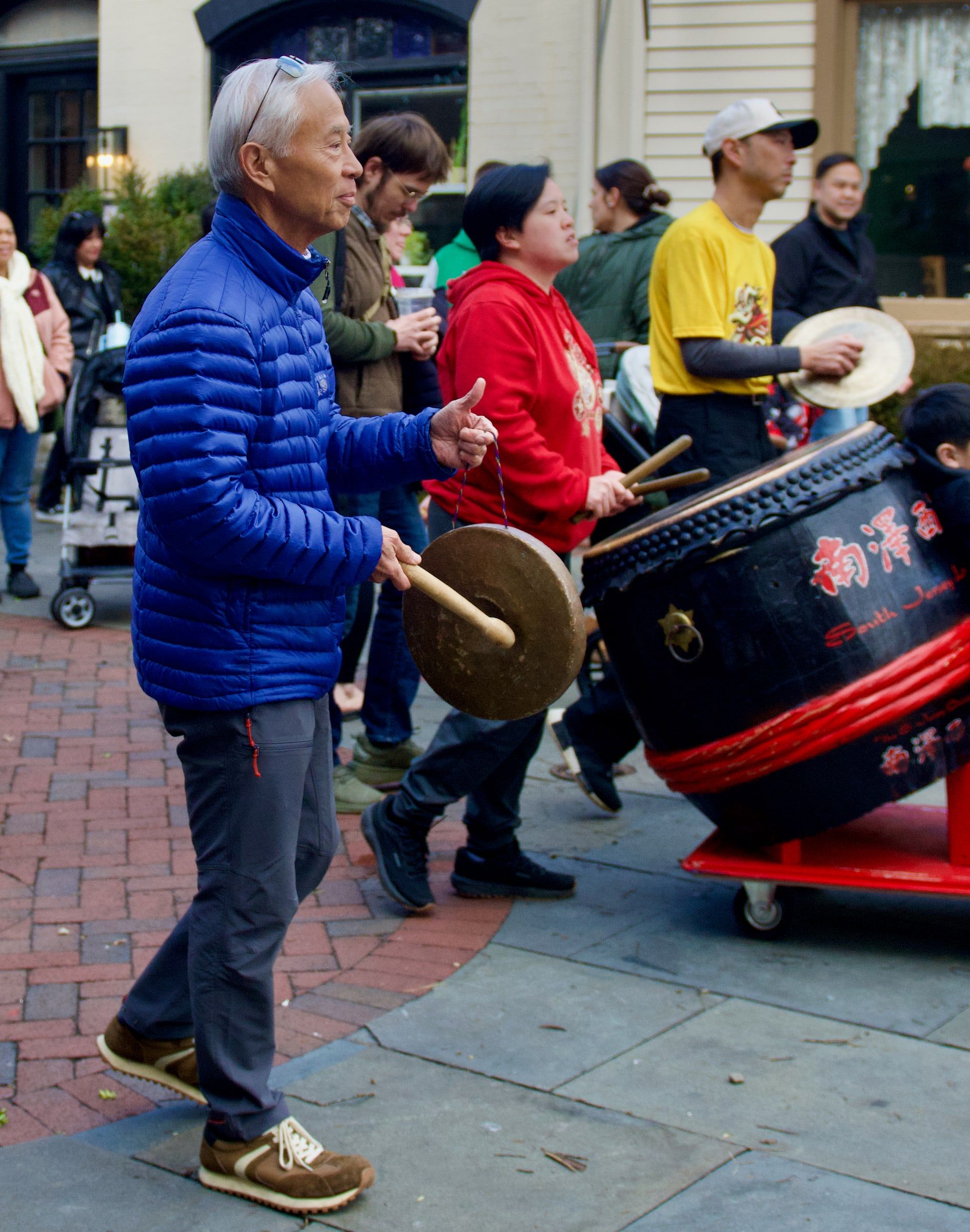 Musicians playing the gong, cymbals and lion dance drum on a brick sidewalk
