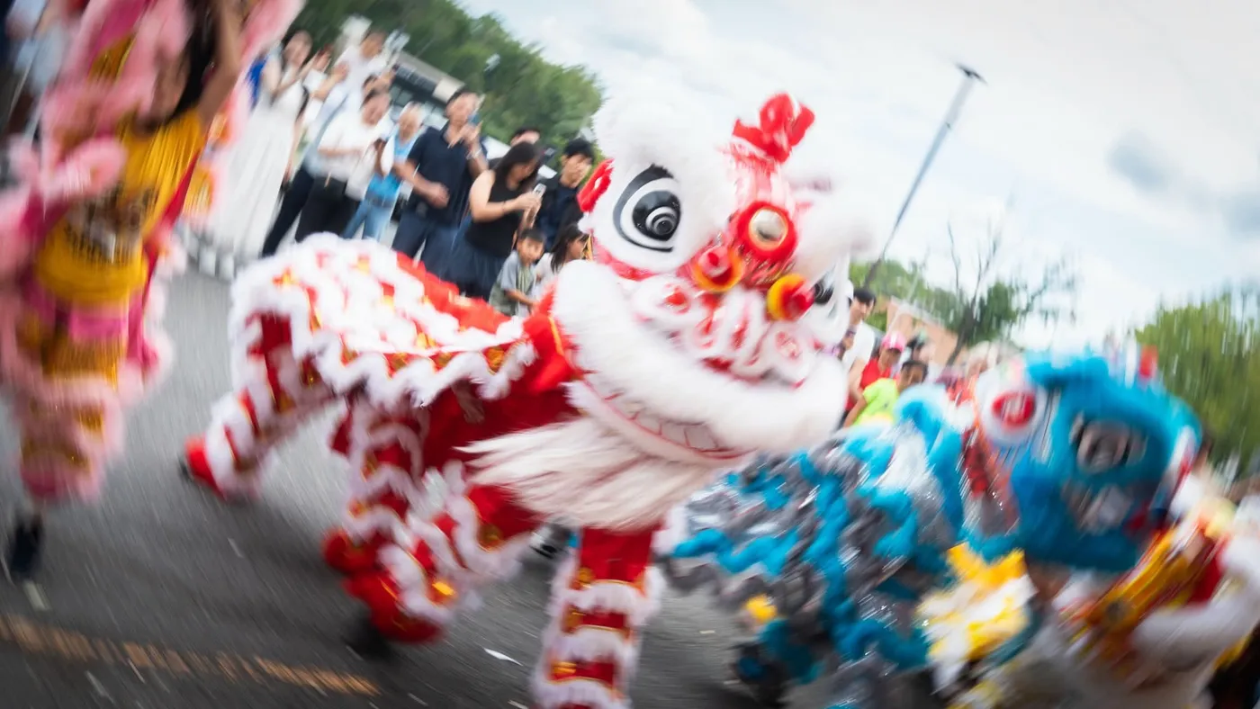 A red and white lion dancing down a parade route, blurred with motion