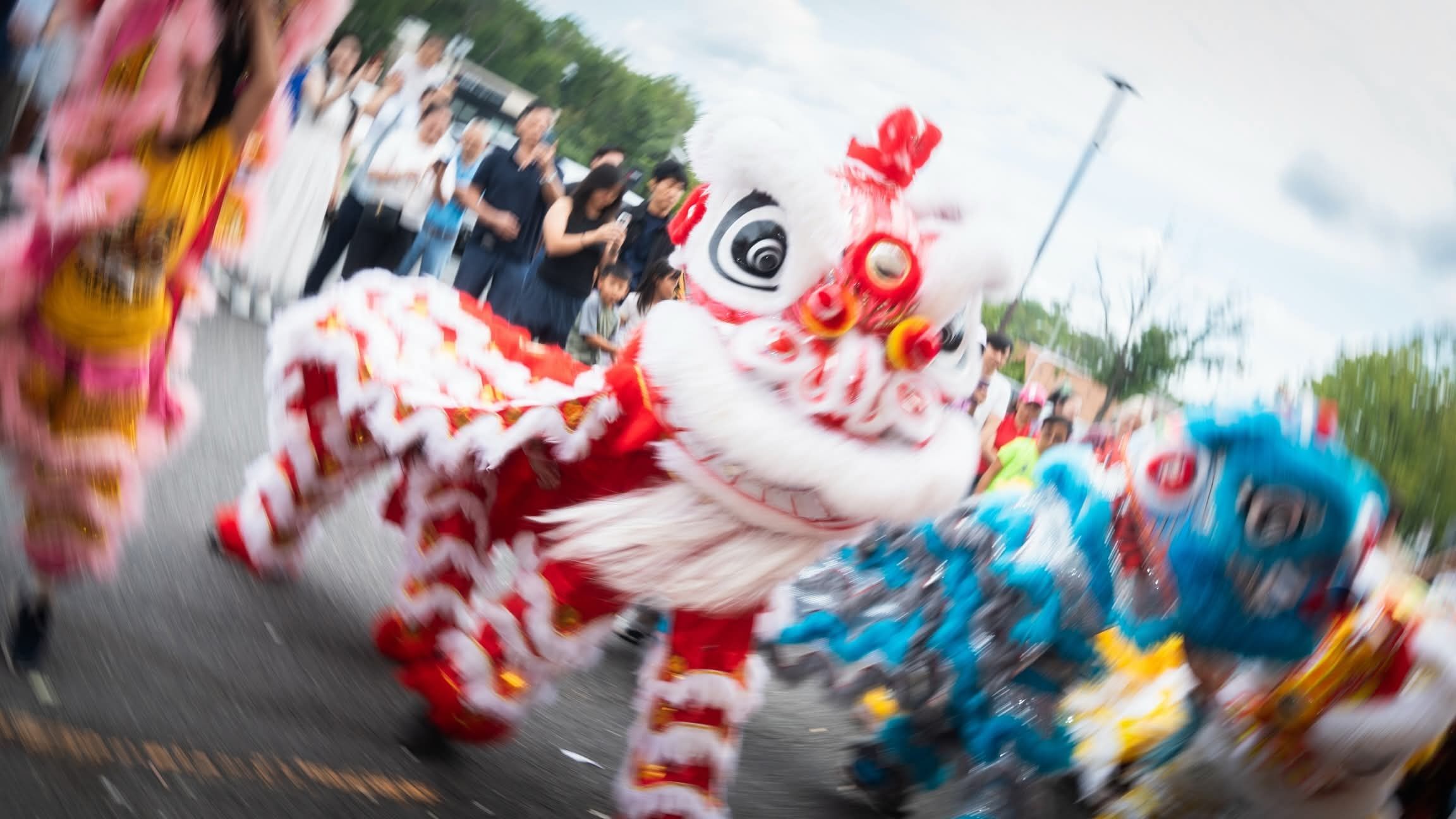 A red and white lion dancing down a parade route, blurred with motion
