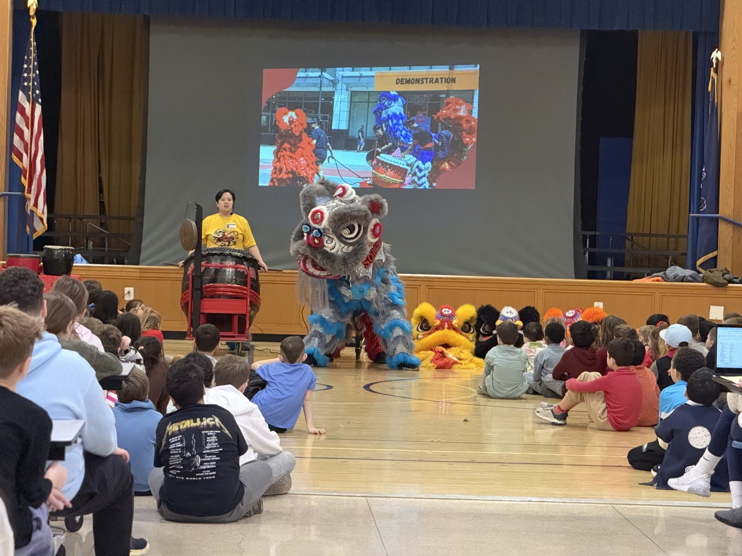 A troupe member presenting a lion dance demonstration to students in a school gym