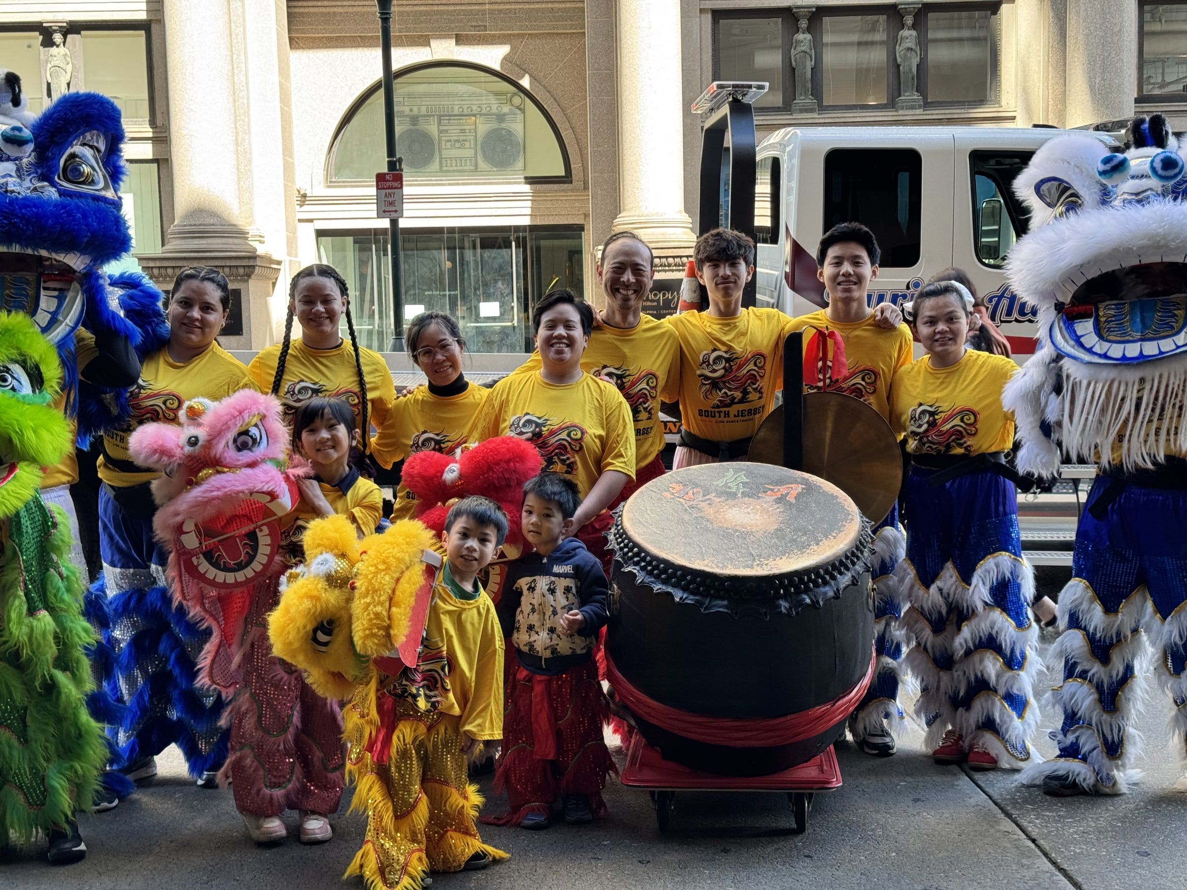 Troupe members in yellow shirts posing with their lions and drum on a city street