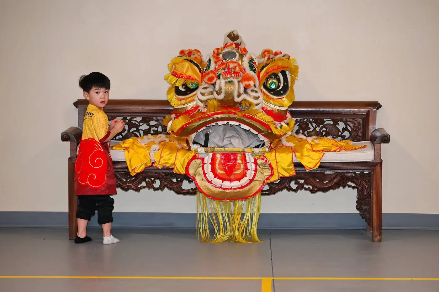 A toddler standing beside a golden lion head resting on a carved bench