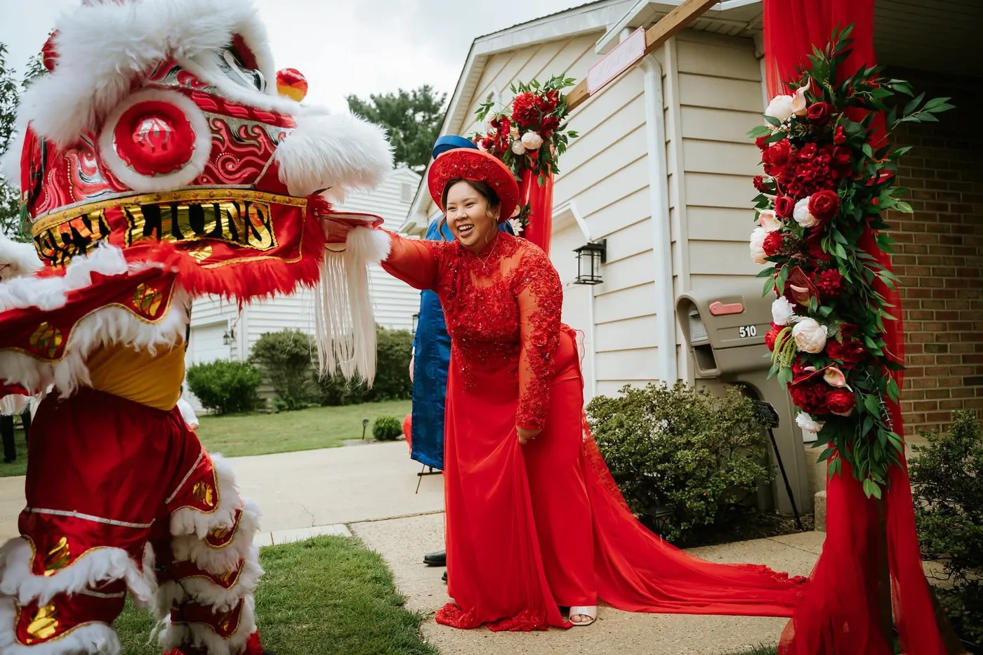 A bride in a red gown laughing as a red and white lion greets her