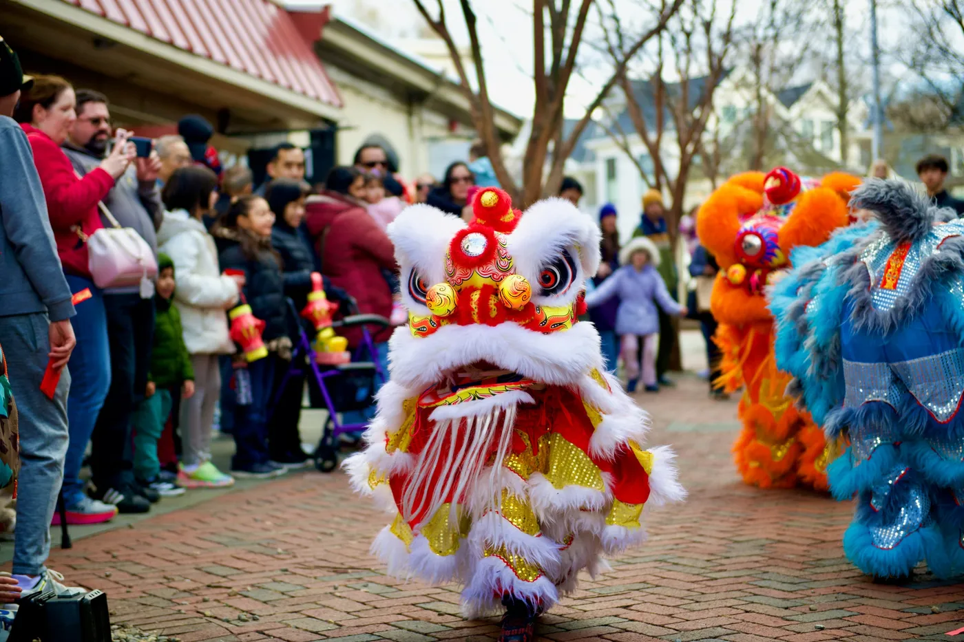 A white and red lion dancing in front of a crowd of families